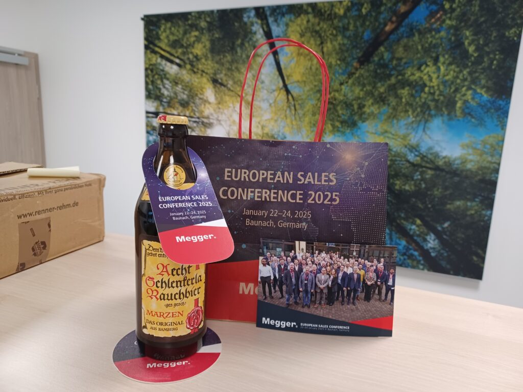 Auf einem Tisch steht eine Flasche mit einem gestalteten Anhänger und eine Tragetasche der Firma Megger