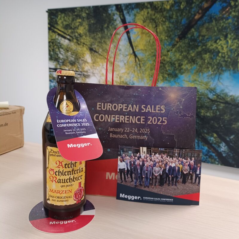 Auf einem Tisch steht eine Flasche mit einem gestalteten Anhänger und eine Tragetasche der Firma Megger
